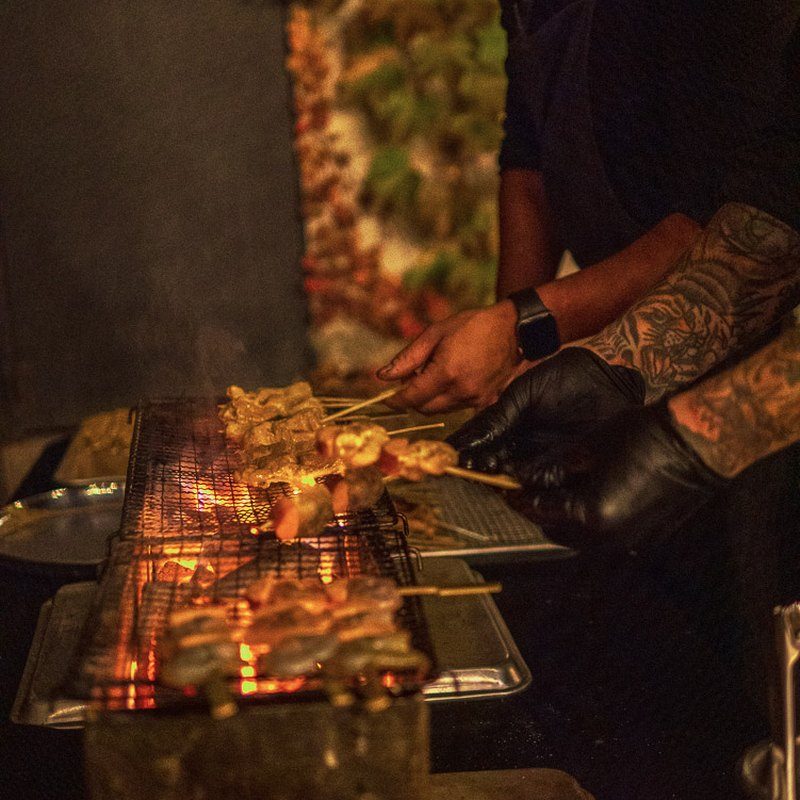 A Vendador chef grilling skewers over a live robata grill